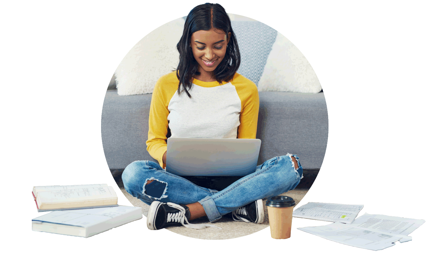 uma jovem sentada estudando e sorrindo em meio a livros, papéis e um computador em seu colo