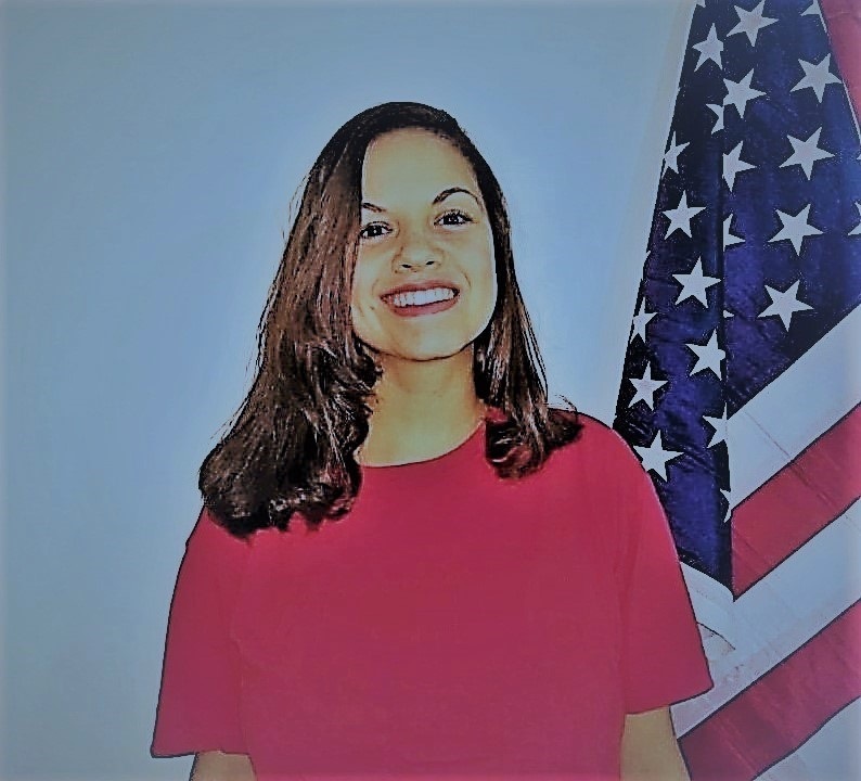 foto da professora de idiomas Josiane Lima sorrindo ao lado de uma bandeira dos Estados Unidos